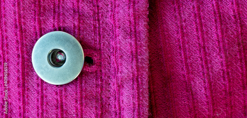 Macro view of silver metal button and woven pink fabric