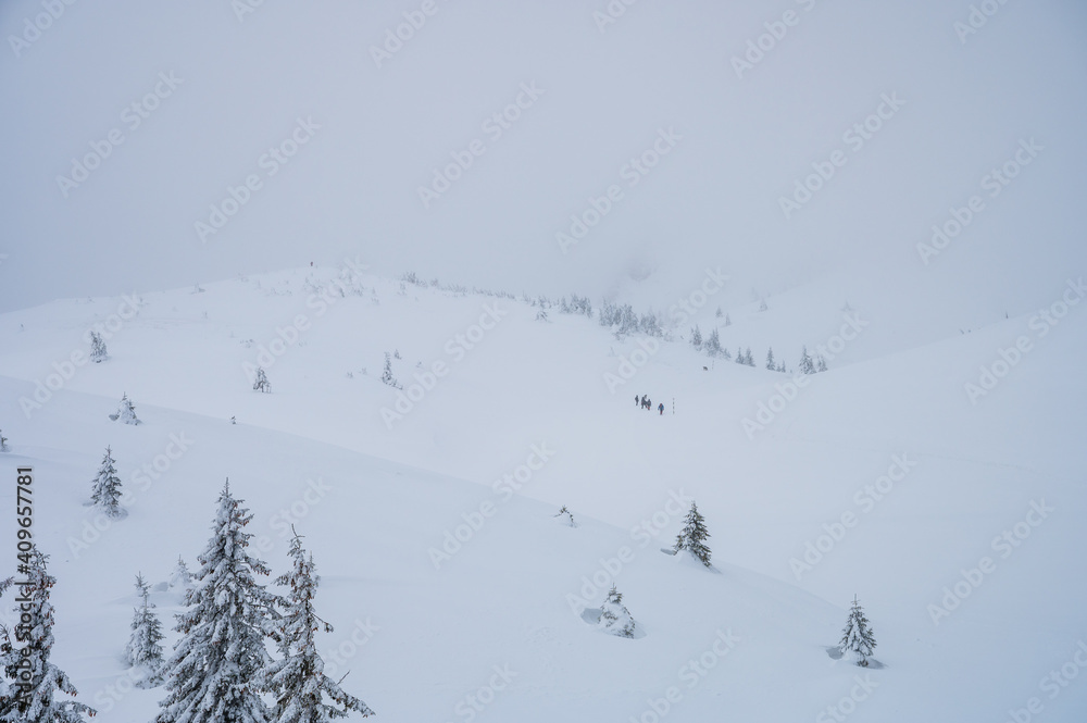 Group of hikers climbing up snow covered Ciucas mountains in winter