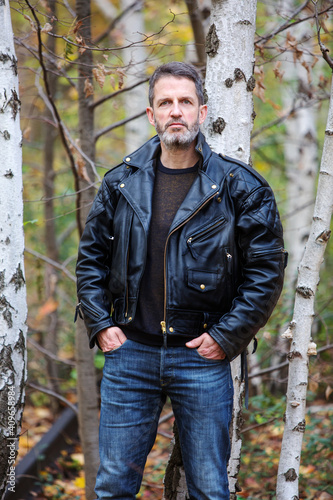 handsome man in leather jacket standing in forest