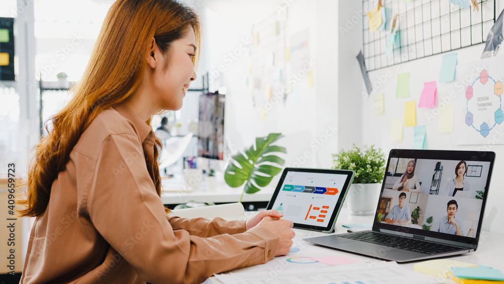 © tirachard - Asia businesspeople using laptop talk to colleagues discussing business brainstorm about plan in video call meeting in new normal office. Lifestyle social distancing and work after corona virus.