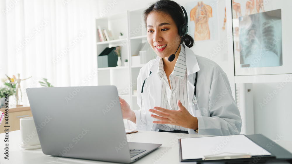 Young Asia lady doctor in white medical uniform with stethoscope using computer laptop talking video conference call with patient at desk in health clinic or hospital. Consulting and therapy concept. Young Asia lady doctor in white medical uniform with stethoscope using computer laptop talking video conference call with patient at desk in health clinic or hospital. Consulting and therapy concept.