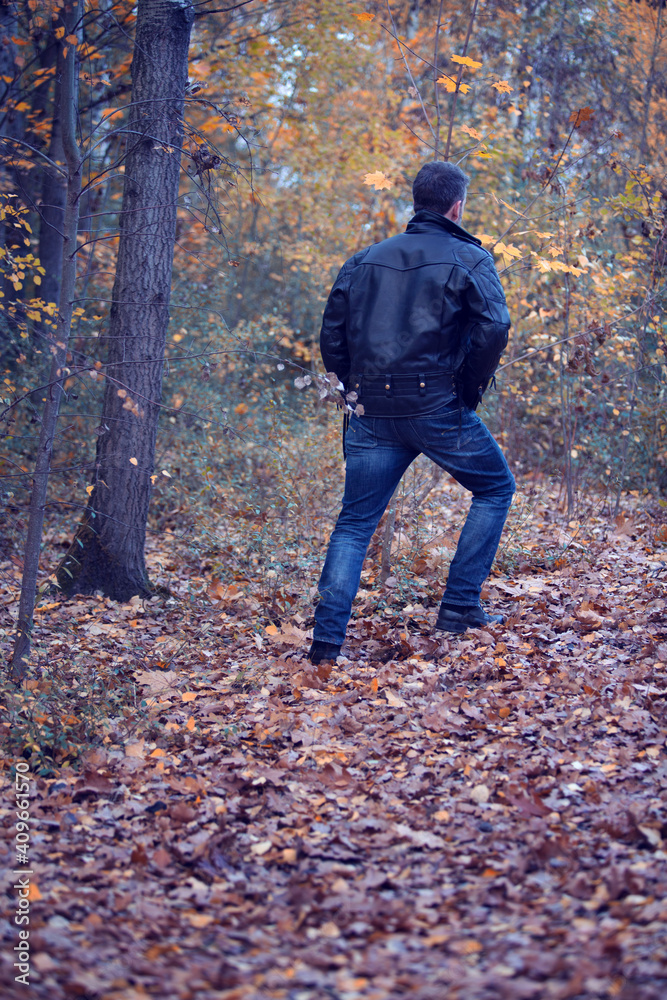 back of man in black leather jacket walking in the forest back of man in black leather jacket walking in the forest