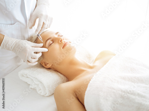 Beautician doctor hands doing beauty procedure to female face with syringe in sunny clinic. Cosmetic medicine and surgery, beauty injections concept