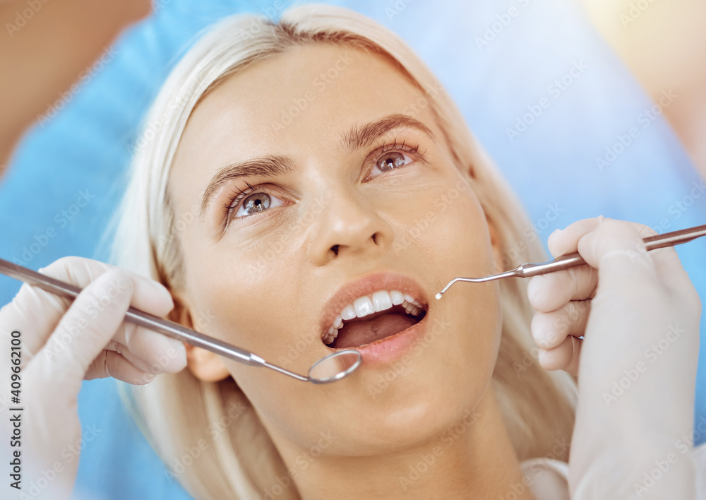 Smiling blonde woman examined by dentist at sunny dental clinic. Healthy teeth and medicine concept