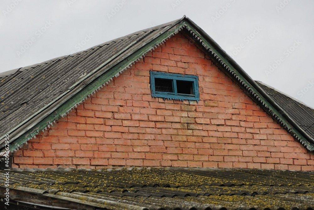 old red brick loft of a rural house with a small blue window under a gray slate roof against the sky old red brick loft of a rural house with a small blue window under a gray slate roof against the sky