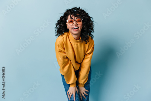 Laughing woman in sunglasses looking at camera. Front view of good-humoured girl in yellow sweatshirt.