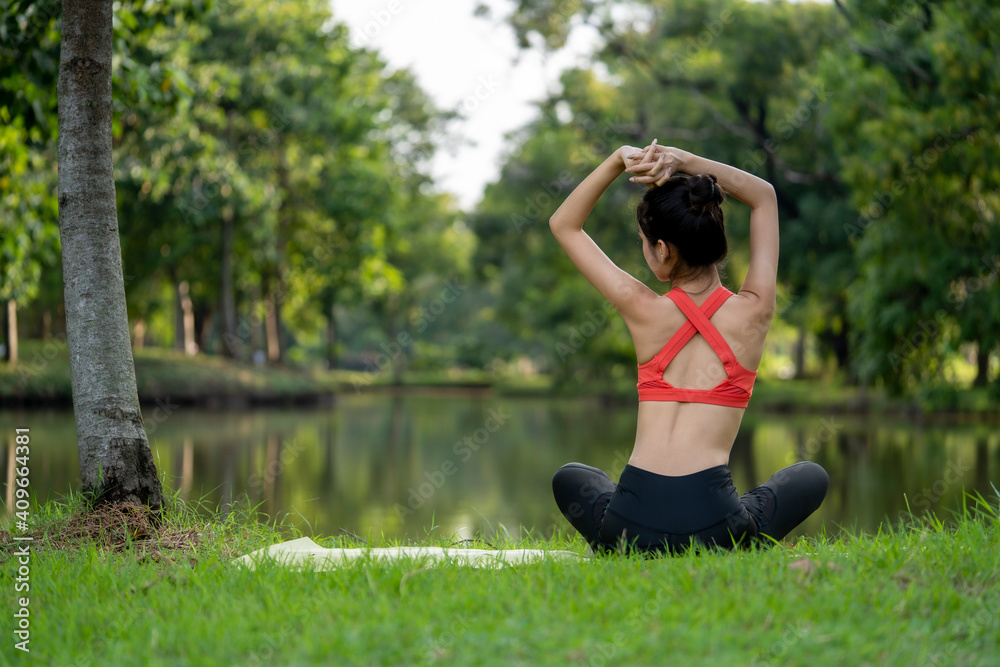 The young Asian woman is feeling good after the morning exercise in the park. She’s cooling down her body by the pond The young Asian woman is feeling good after the morning exercise in the park. She’s cooling down her body by the pond