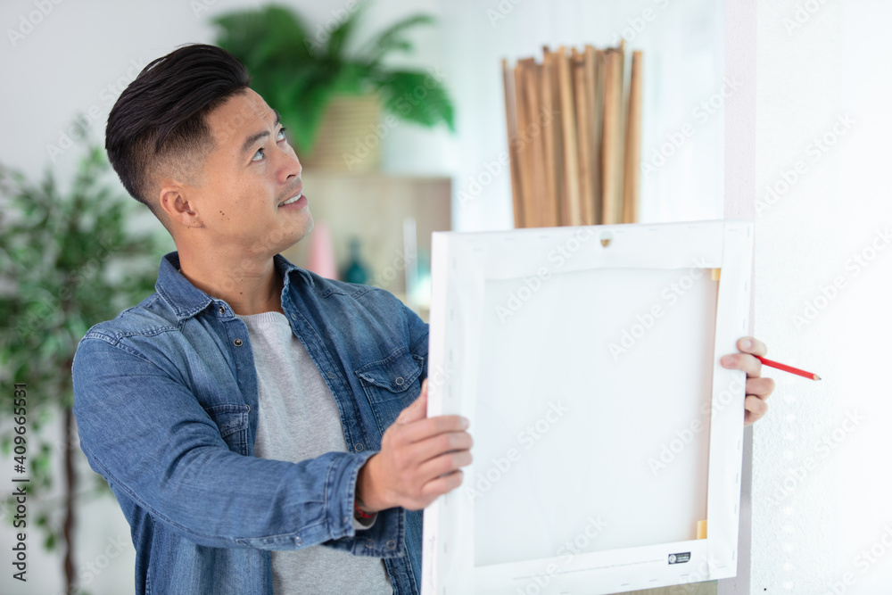 asian man deciding where to hang painting in the home