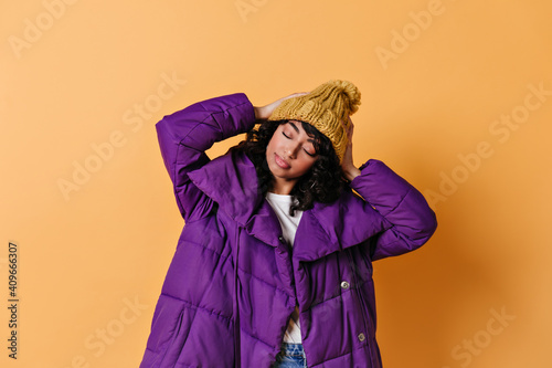 Relaxed mixed race girl posing with closed eyes. Studio shot of winsome young woman in down jacket. © Look!