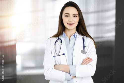 Smiling young woman-doctor is standing in sunny clinic indoors