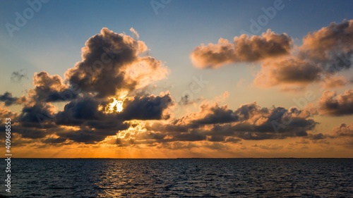 Orange light shining through dramatic clouds over blue German north sea at sunset