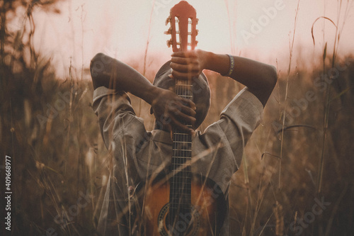 man holding classical guitar while sitting on grass field during sunset 