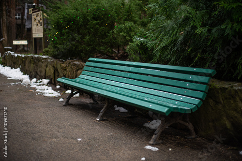 Green, wet, vacant park bench in winter park. Shallow depth of field image.
