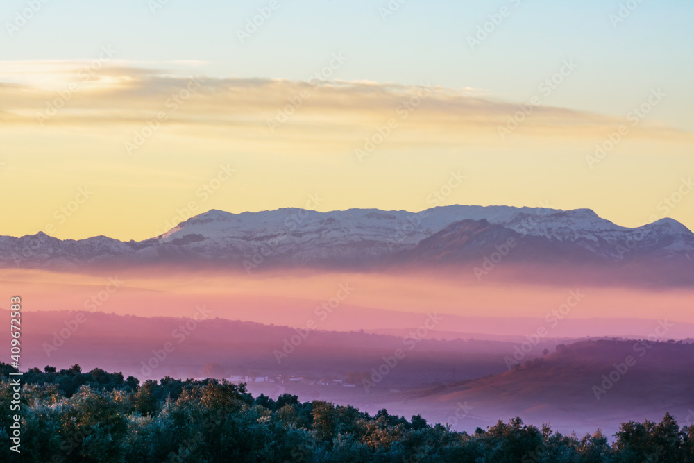 Landscape of Sierra Morena de Jaen, located in the northern region of Linares, with snow-capped mountains and the morning mist colored by the sun.