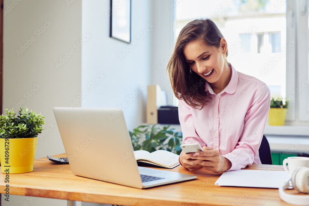 Young woman working from home texting on mobile phone Young woman working from home texting on mobile phone
