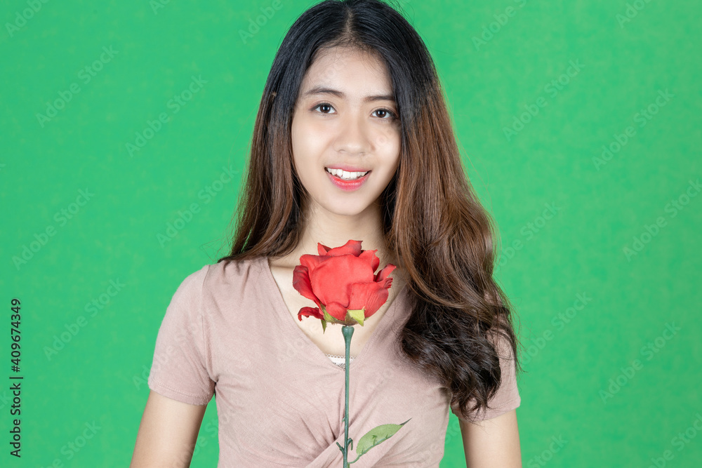 Attractive young Asian woman holding rose over green isolated background. Love and Valentines day Attractive young Asian woman holding rose over green isolated background. Love and Valentines day