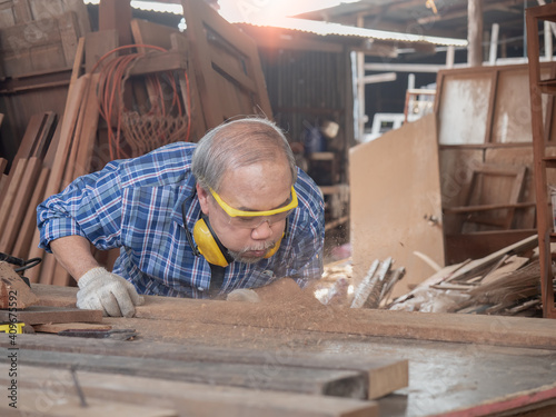 Elderly carpenter craftsman working with hardwood in the workshop and blowing off sawdust. Manufacture of wood products...