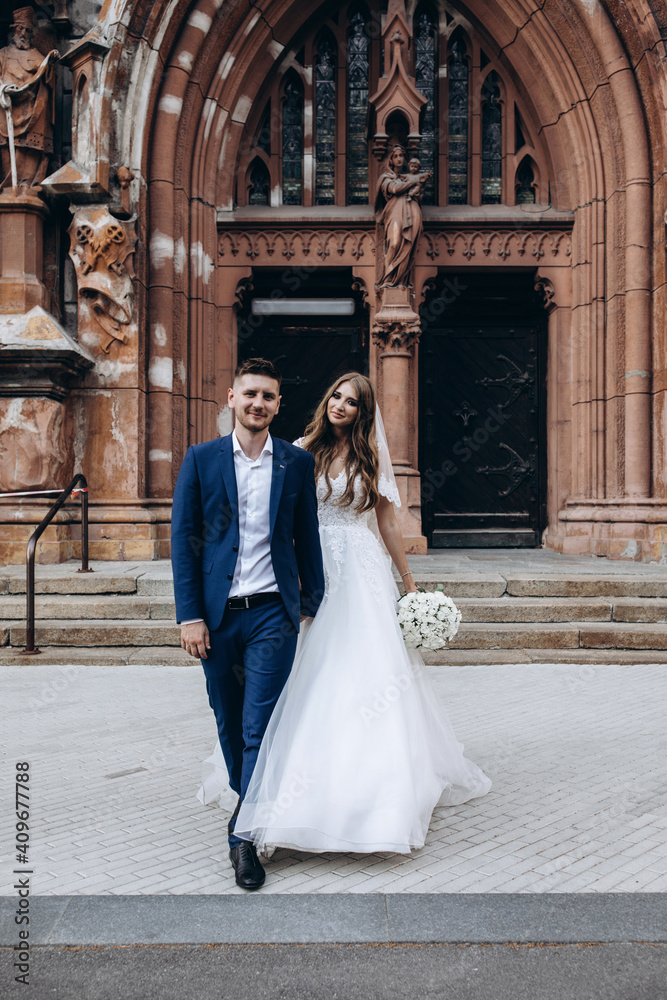 Obraz premium A romantic walk of the bride and groom through the city streets. Newlyweds on the background of the cathedral.