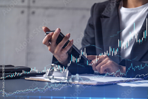 A woman financial trader in formal wear is checking the phone to sign the contract to invest money in stock market. Internet trading and wealth management concept. Forex hologram chart.