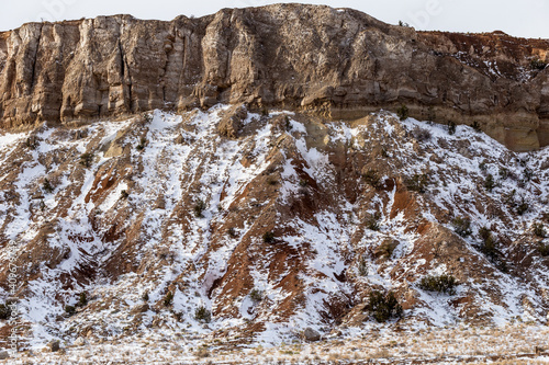 Side of tall red rock mountain covered in snow on overcast day in rural New Mexico