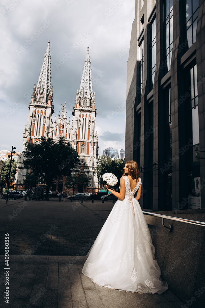Obraz premium The bride in a white dress is holding a beautiful wedding bouquet. The bride on the background of the old cathedral.