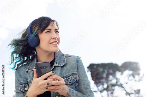woman talking on the phone-brunette woman listening to music from her cell phone with large headphones in the street