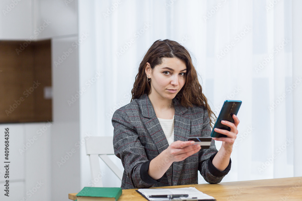 A young attractive woman enters her credit card details through an app on her phone, shopping online A young attractive woman enters her credit card details through an app on her phone, shopping online