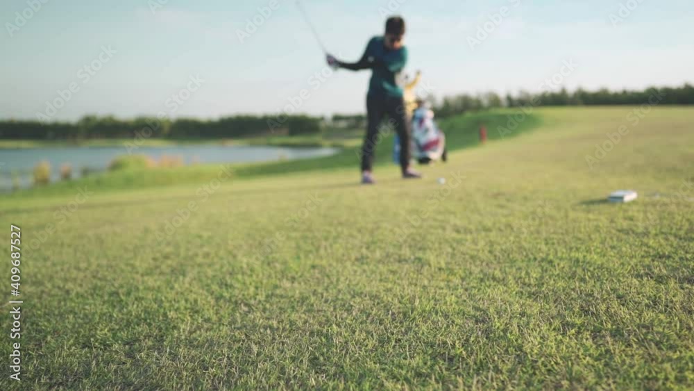 Blue shot focus on the ground - Male golfer player shifting golf on green grass professional golf course on sunset. Golfer with golf club, golfer swinging and hitting golf ball, outdoor recreation	
