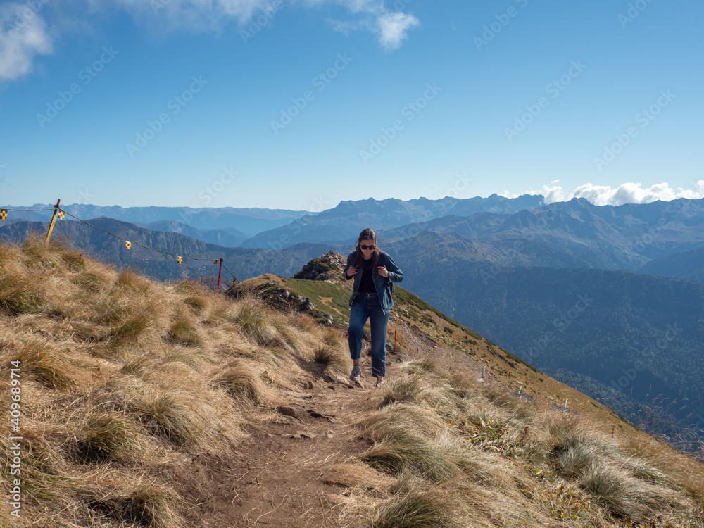young female tourist with a backpack is walking in the mountains, traveling in national parks. Local tourism, beautiful nature, valleys and mountains