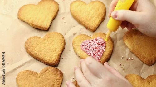 woman decorates heart shaped cookies with yellow icing, close-up, baking process, romantic concept