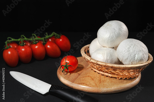 White mushrooms champignons on a wooden tray with a branch of cherry tomato