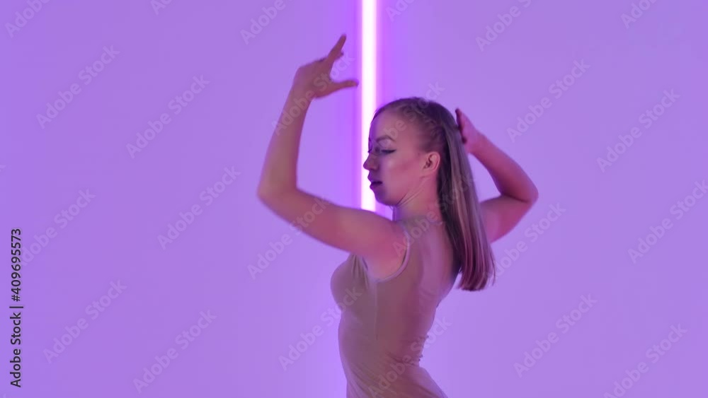 Feminine female dancer performs sensual contempt and jumps gracefully against a backdrop of bright neon lights. Young woman dancing modern choreography in a dark studio. Close up. Slow motion. Feminine female dancer performs sensual contempt and jumps gracefully against a backdrop of bright neon lights. Young woman dancing modern choreography in a dark studio. Close up. Slow motion.