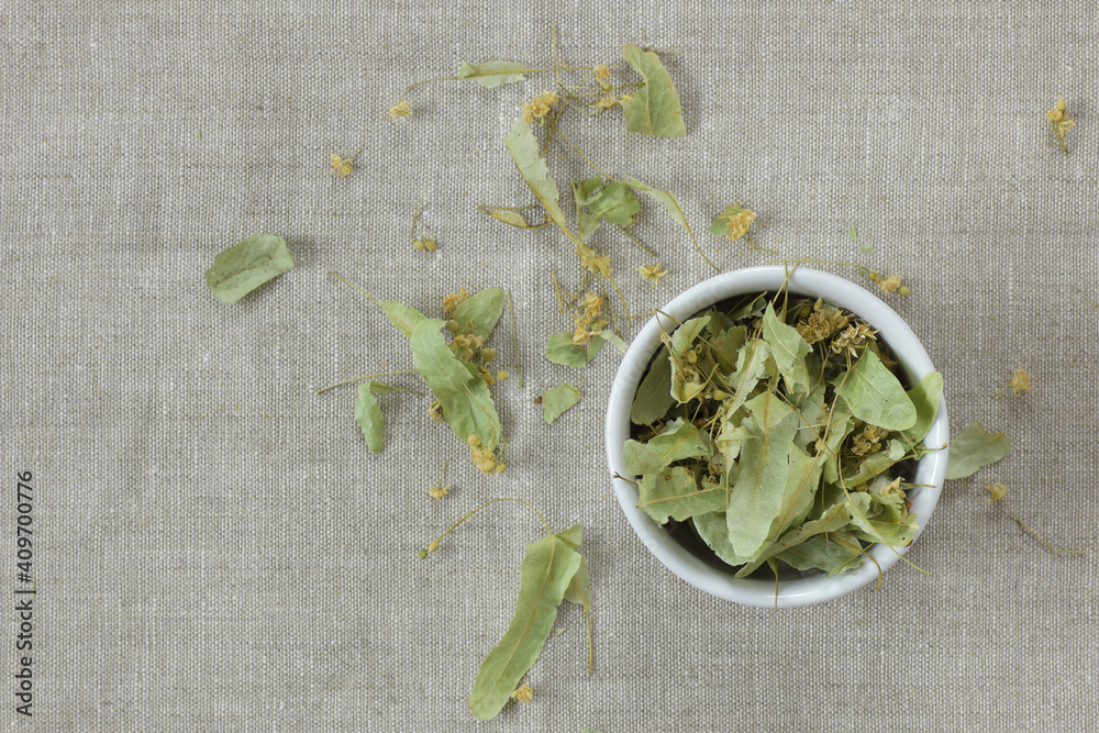 Dried lime-blossoms from above on linen textile with lime leaf flower buds neaby, overhead top view, flat lay, closeup, copy space, herbal tea nad naturopathy concept