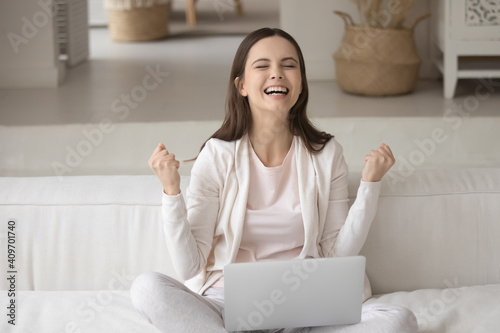 Overjoyed young Caucasian woman sit on sofa at home feel euphoric win online lottery on laptop. Happy excited millennial female triumph read good promotion news on web. Success concept.