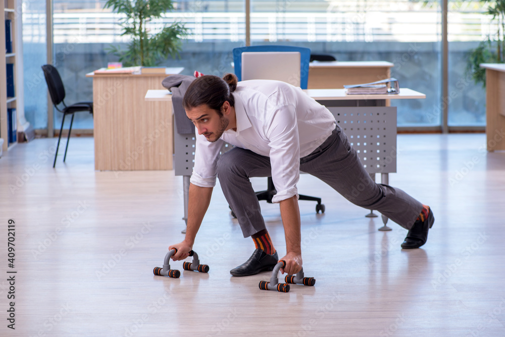 Young male employee doing sport exercises in the office
