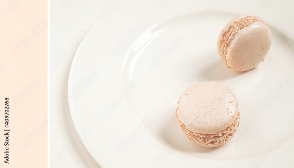 Two light delicious french macaroons on a light plate, trend color 2021 Set Sail Champagne, minimalist composition close-up Two light delicious french macaroons on a light plate, trend color 2021 Set Sail Champagne, minimalist composition close-up