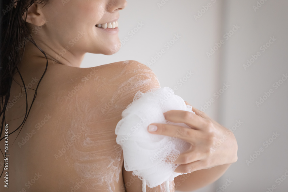Fototapeta premium Crop close up of smiling young Caucasian woman take shower rub massage body with foam gel using puff. Female take care of body hygiene wash in bathroom with natural beauty product. Skincare concept.