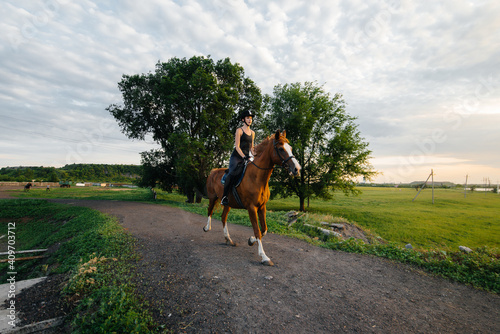 A young pretty girl jockey riding a thoroughbred stallion is engaged in horse riding at sunset. Equestrian sports., horse riding