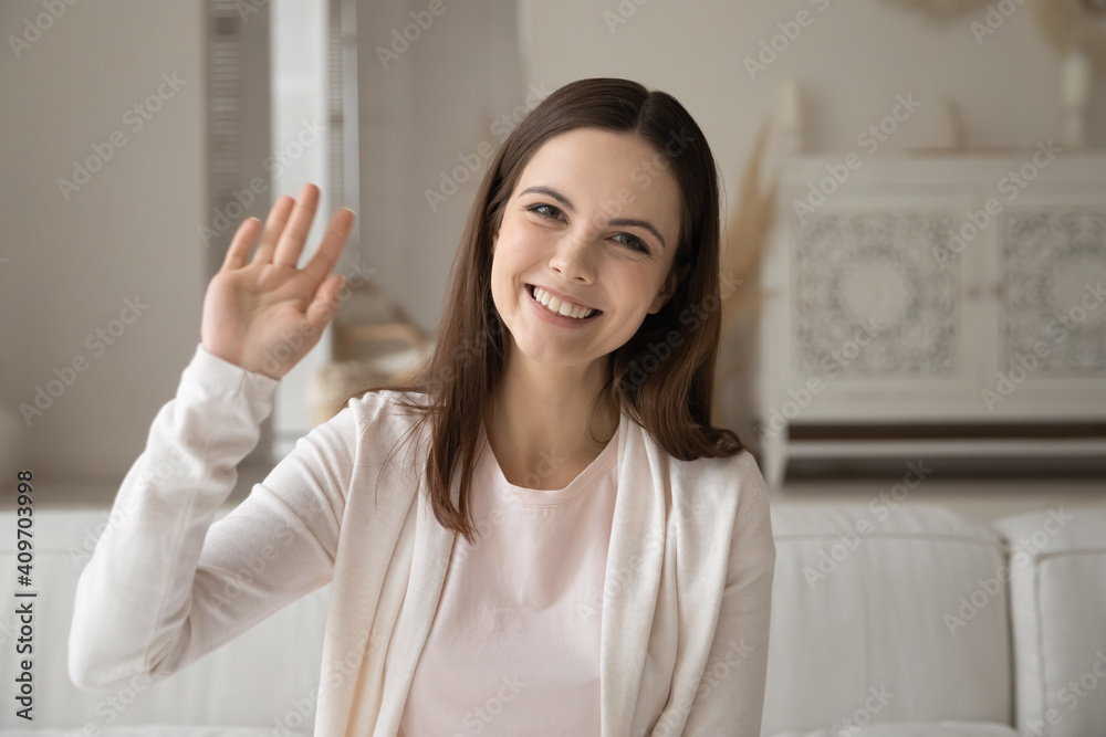 Close up portrait of smiling millennial Caucasian woman sit on couch at home wave greet talking on video call. Happy young female have fun speak on webcam digital virtual conference using internet. Close up portrait of smiling millennial Caucasian woman sit on couch at home wave greet talking on video call. Happy young female have fun speak on webcam digital virtual conference using internet.