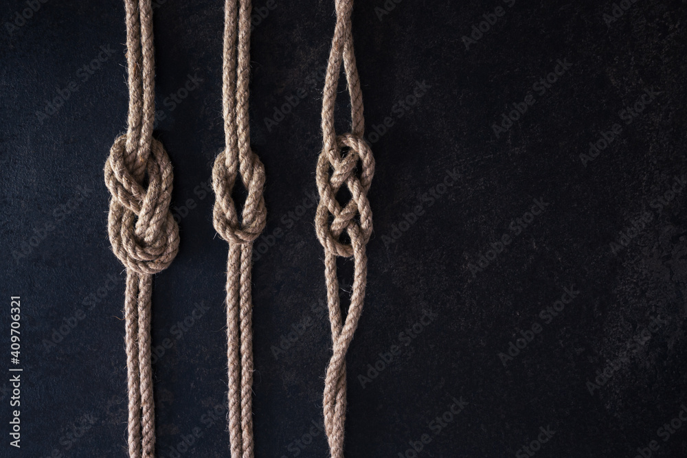Flat lay set of three nautical knots tied on natural ropes. Ropes are parallel on a dark background Flat lay set of three nautical knots tied on natural ropes. Ropes are parallel on a dark background