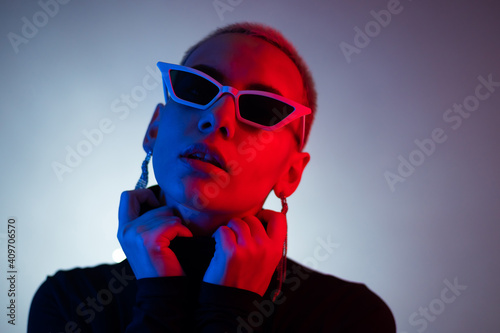 Portrait of a young woman with a short male haircut in sunglasses in neon light in the studio © Михаил Решетников