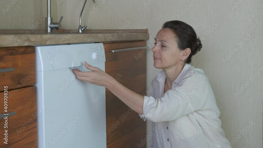 Clean dishes in a machine. A woman look into a dishwasher full of utensils in it in the kitchen. Clean dishes in a machine. A woman look into a dishwasher full of utensils in it in the kitchen.