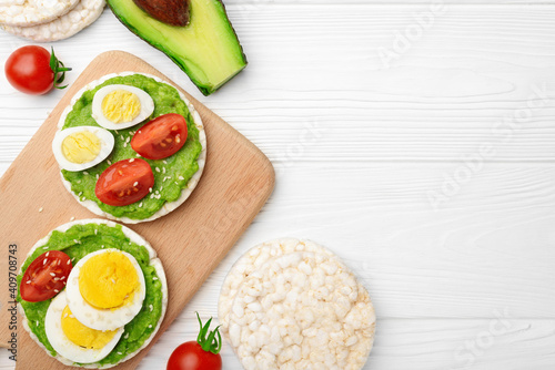 Top view rice cakes with avocado mash and eggs with tomato on wooden background with copy space