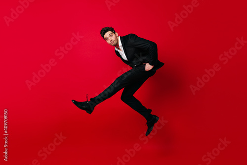Carefree boy in black suit dancing. Jumping man looking at camera.