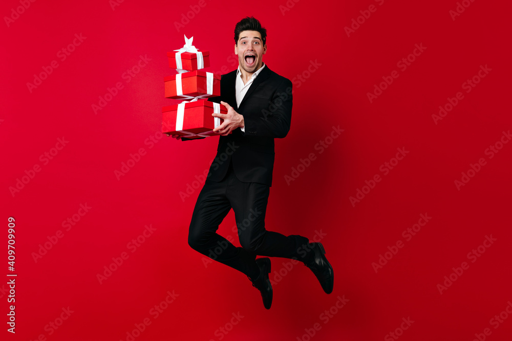 Well-dressed male model posing with presents. Funny young man jumping on red background. Well-dressed male model posing with presents. Funny young man jumping on red background.