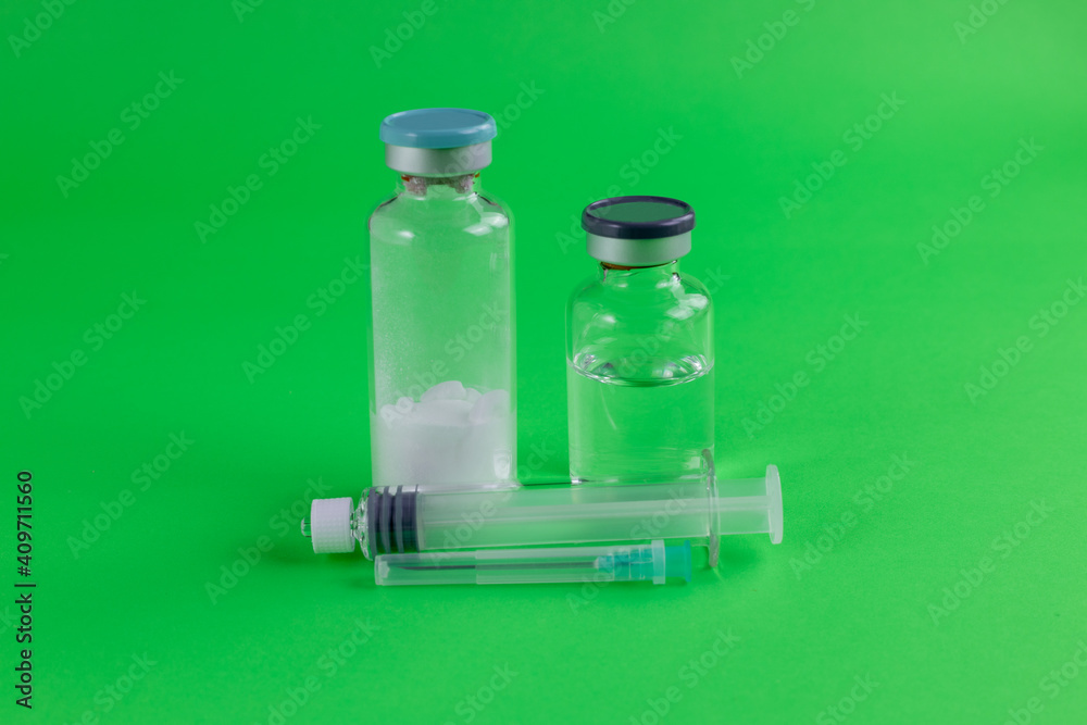 covid 19 vaccine drug bottles and syringe with needle, green background