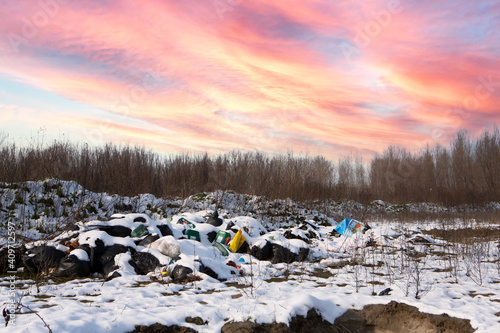 Ecological crisis. Different garbage and trash on snow at beautiful winter forest at colorful sky. Environmental pollution by garbage. Destructive human influence on nature © cnikola