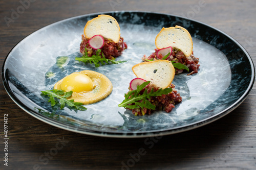 beef tartare with egg, white bread croutons and fresh radish. scrambled eggs with glaze. on a blue marble plate
