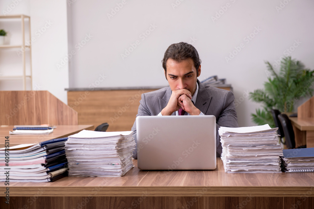 Young male employee unhappy with excessive work in the office Young male employee unhappy with excessive work in the office