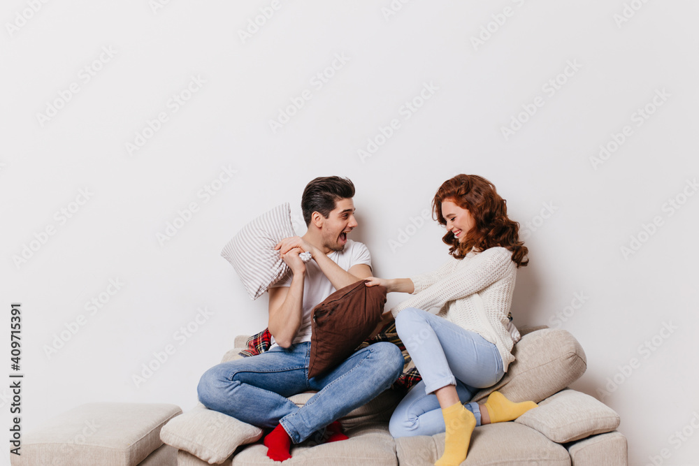 Ginger girl sitting on couch with boyfriend. Indoor shot of couple posing during pillow fight. Ginger girl sitting on couch with boyfriend. Indoor shot of couple posing during pillow fight.